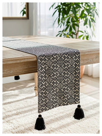 Black and white patterned table runner with tassels on a wooden table.