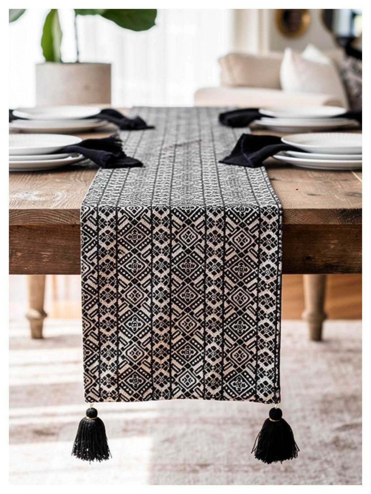 Table runner with black and white pattern and tassels on a wooden table.