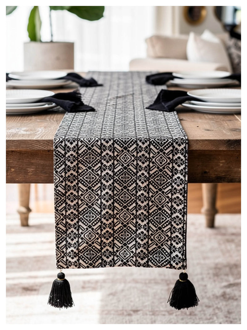 Table runner with black and white pattern and tassels on a wooden table.