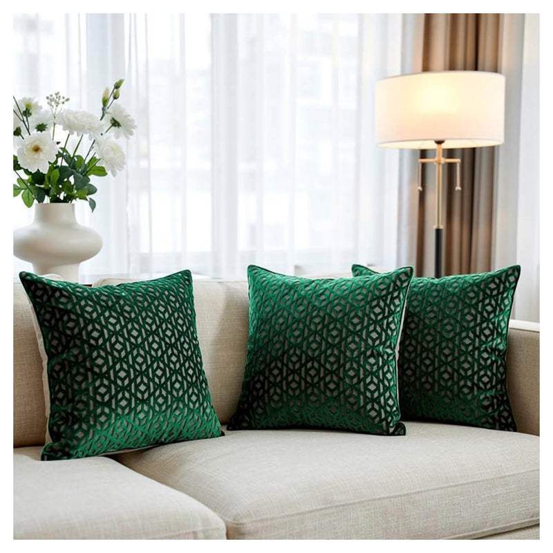 Green patterned pillows on a beige sofa with a lamp and flowers in the background