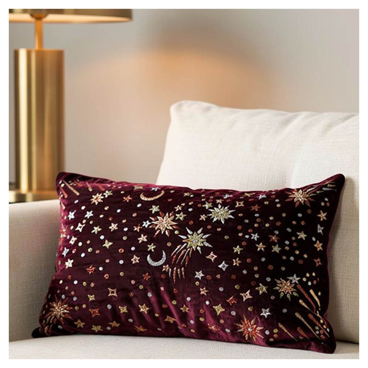 Crimson starburst lumbar pillow with gold, rose gold and champagne metallic embroidery styled on a couch