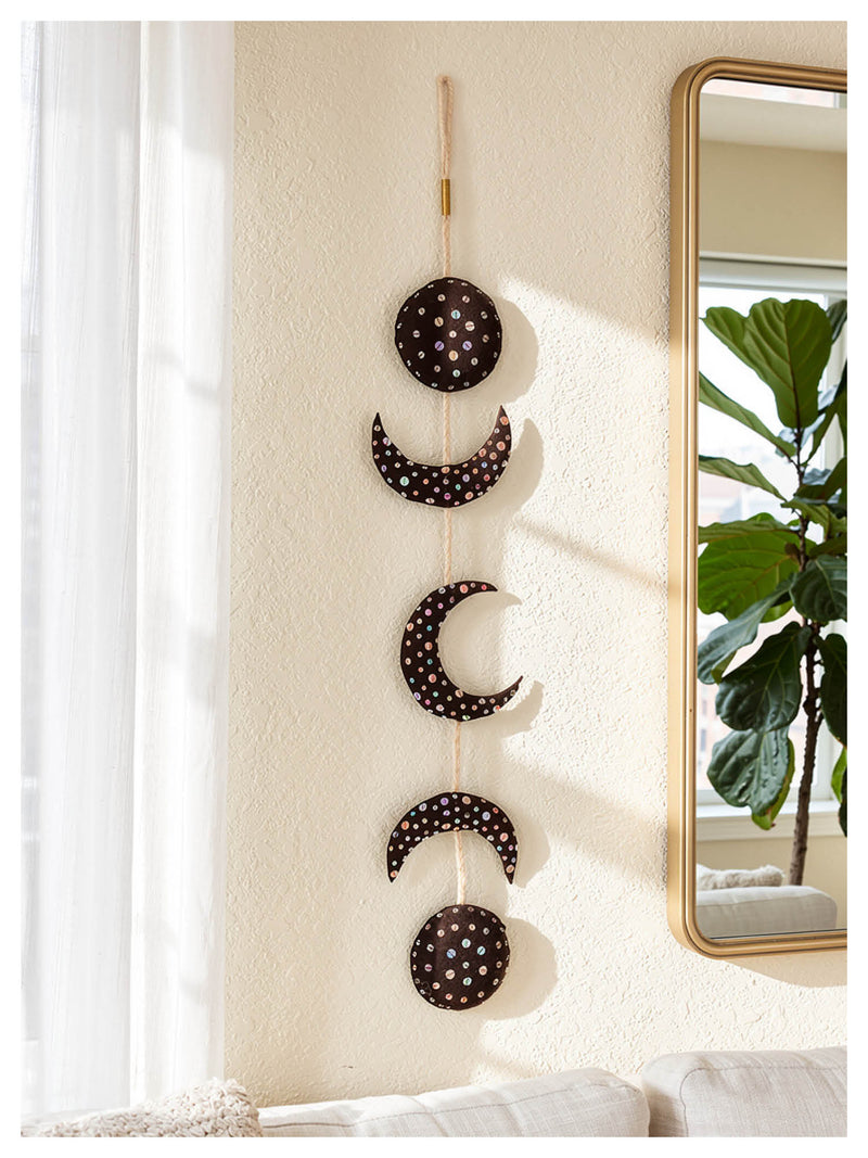 Decorative wall hanging with moon phases on a neutral wall next to a mirror.