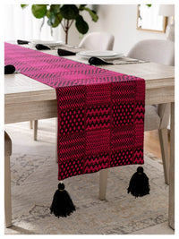 Pink and black patterned table runner with tassels on a dining table.