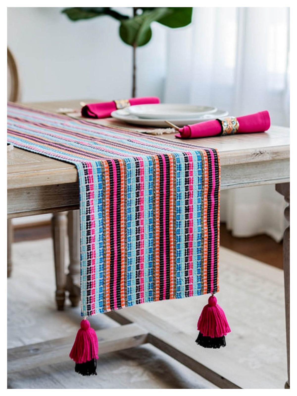 Colorful striped table runner with tassels on a wooden table.