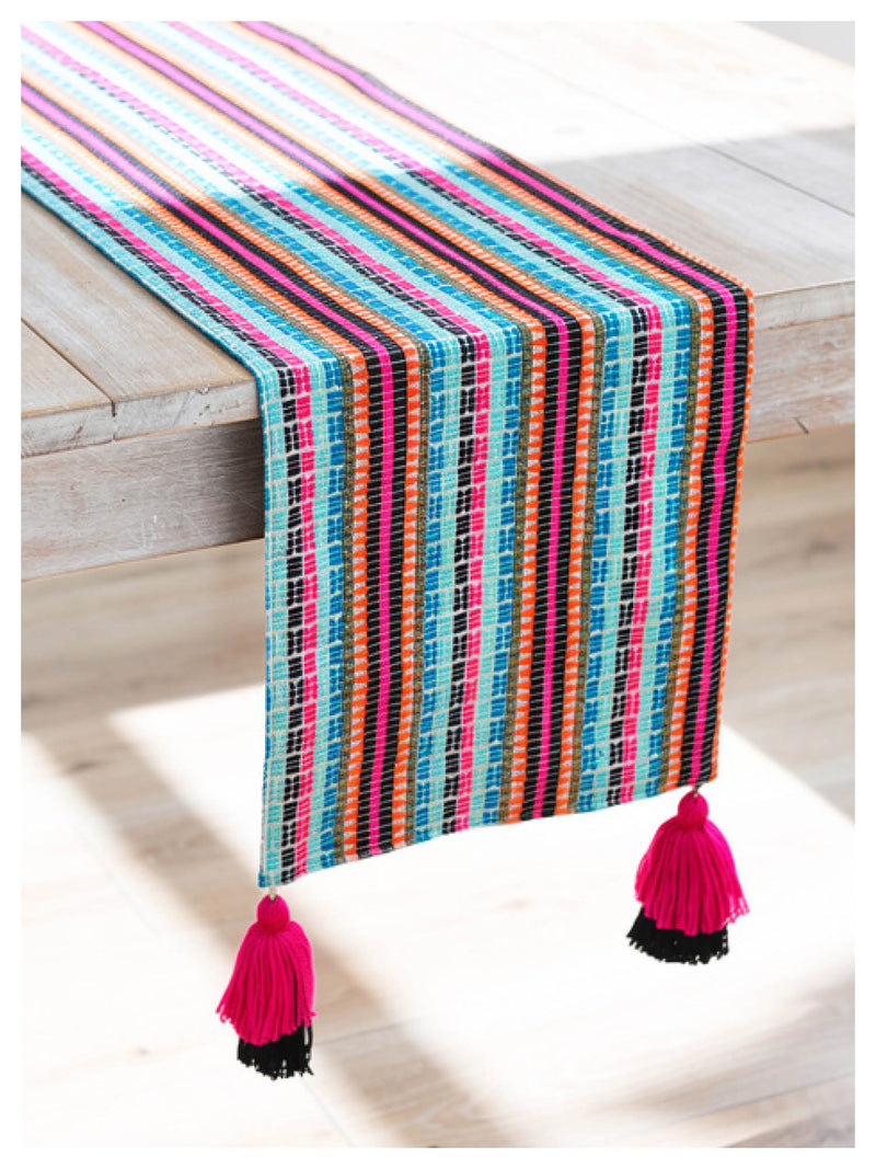 Colorful striped table runner with tassels on a wooden surface