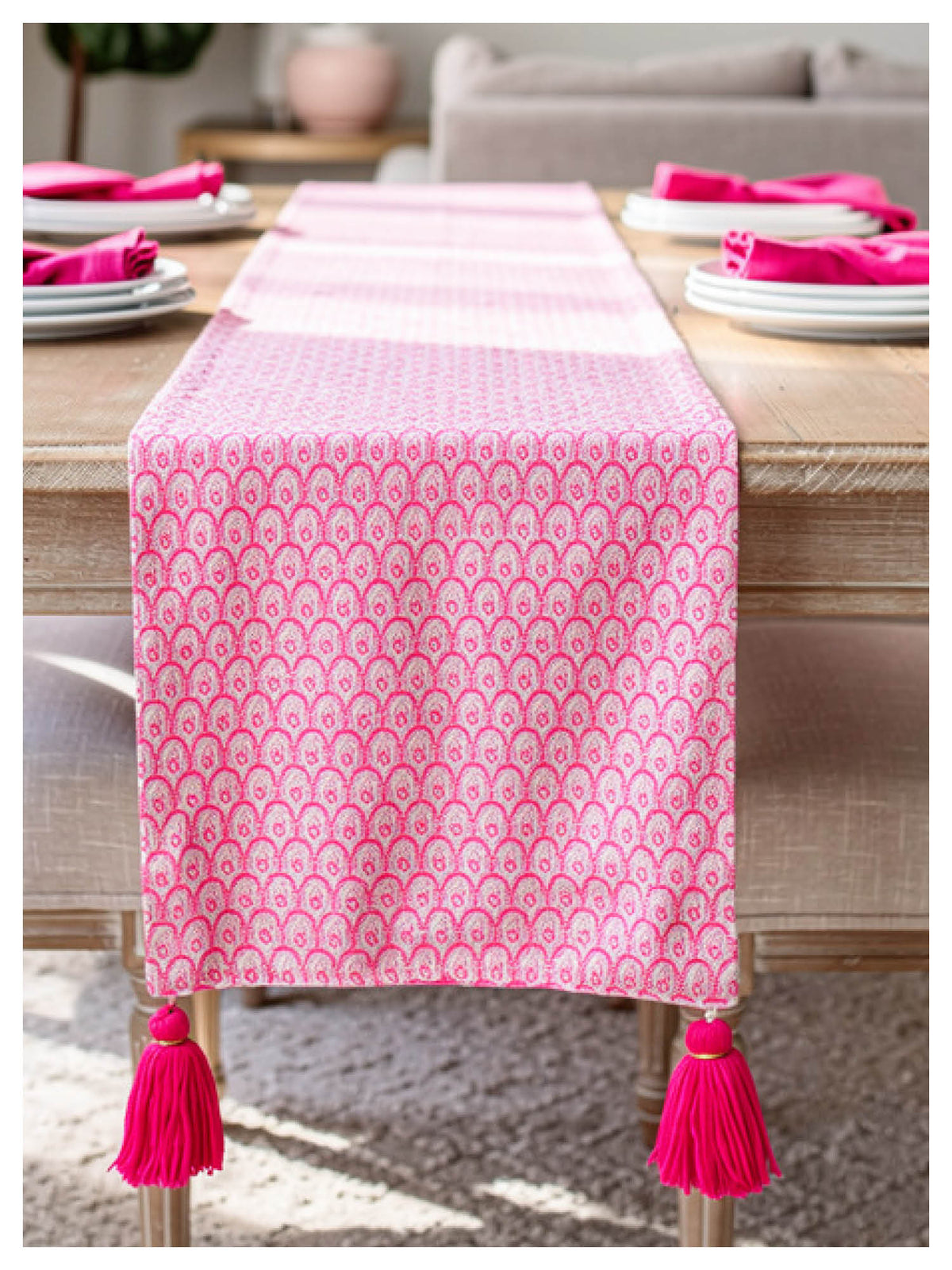 pink scallop decorative table runner with tassels on a wooden table
