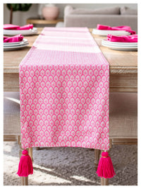 pink scallop decorative table runner with tassels on a wooden table

