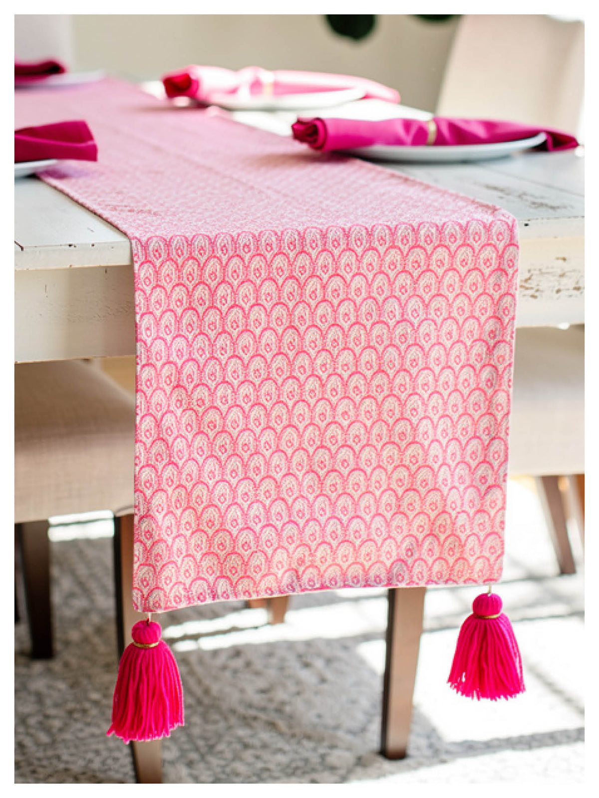Pink patterned table runner with tassels on a dining table.