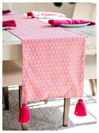 Pink patterned table runner with tassels on a dining table.