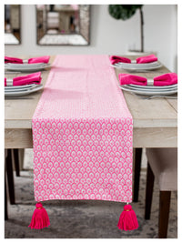Pink patterned table runner with tassels on a dining table.