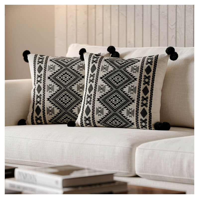 Two decorative pillows with black patterns and pom-pom edges on a white couch.