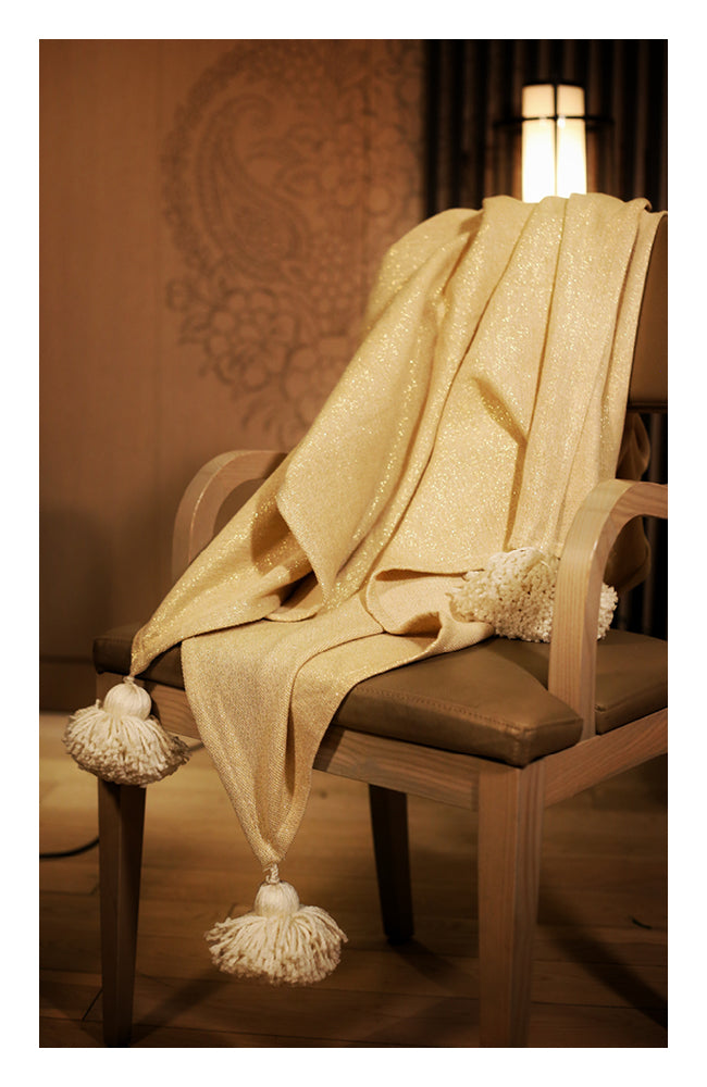Off-white and gold throw with tassels styled on a neutral sofa